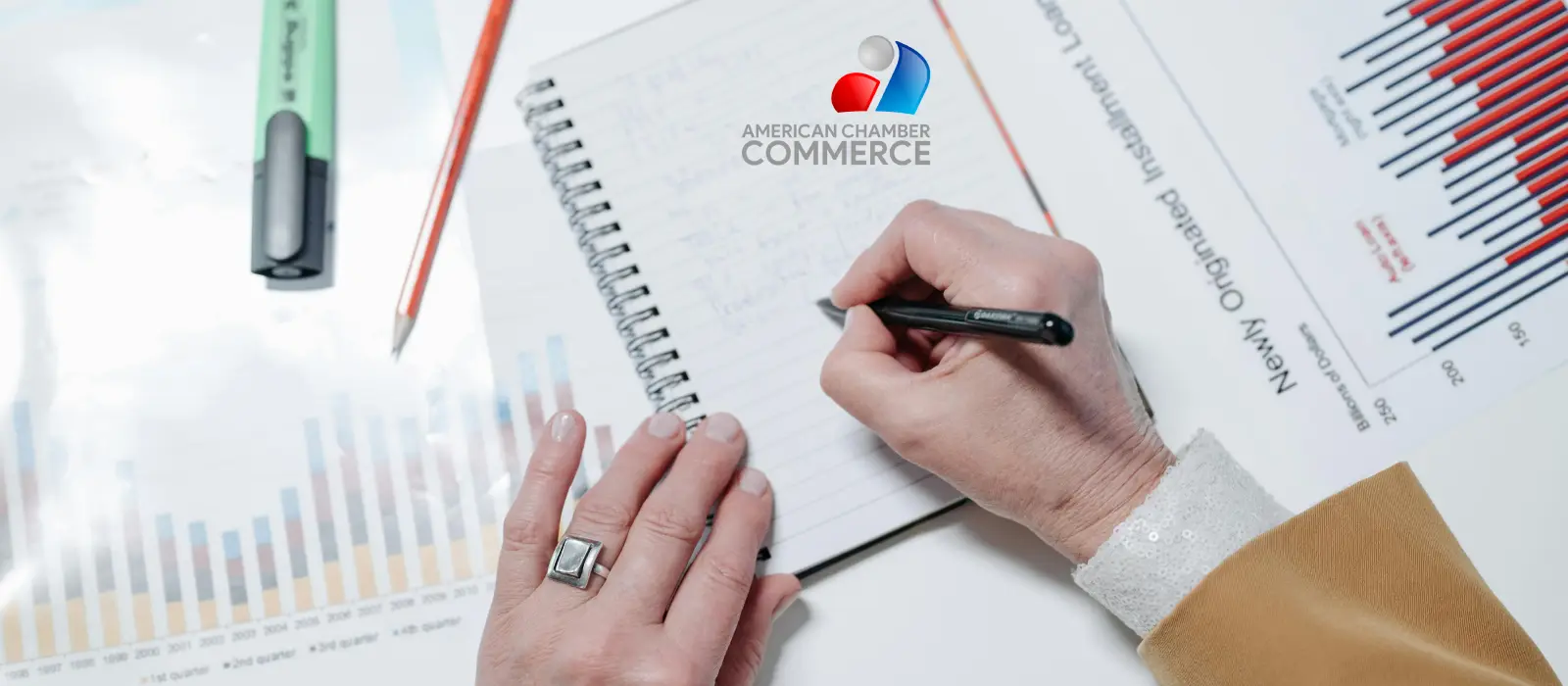Hands writing notes beside printed business charts